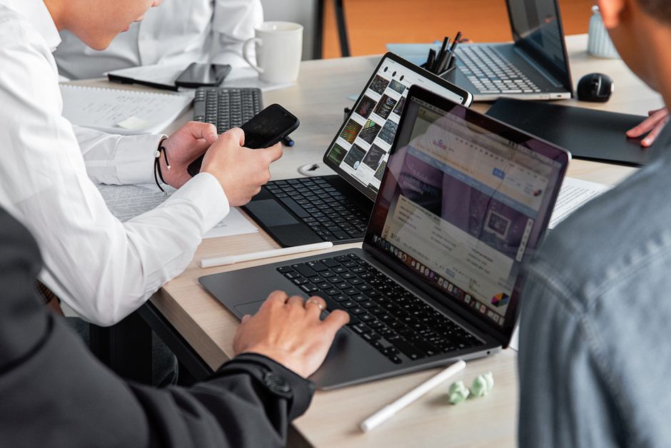 Professionals in a modern office discussing work with laptops and smartphones